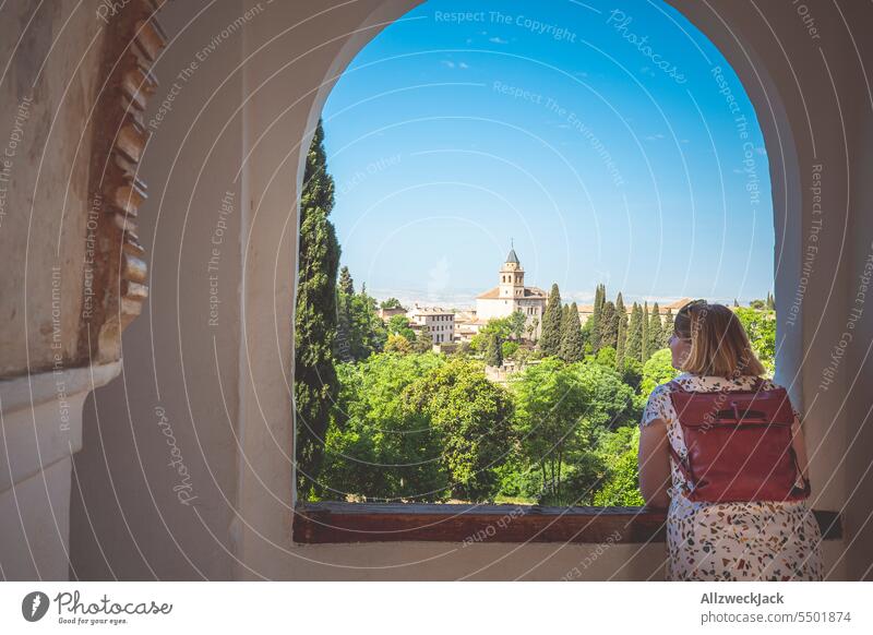 middle-aged caucasian woman with blond hair and backpack on her back looks out of window at picturesque scenery in Andalusia Spain Andalucia Granada Summer