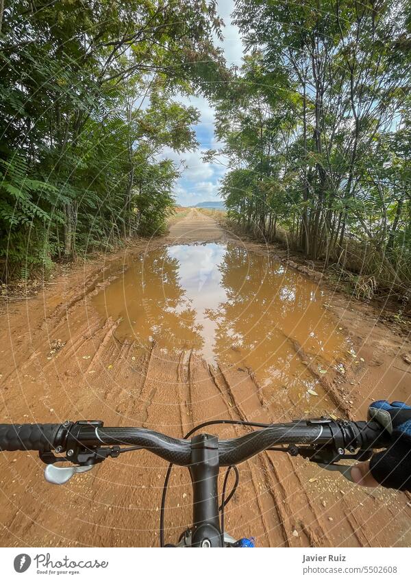 first person view of the handlebars of a mountain bike just before crossing a large puddle of mud and water on a path through a forest pond patch rain clay