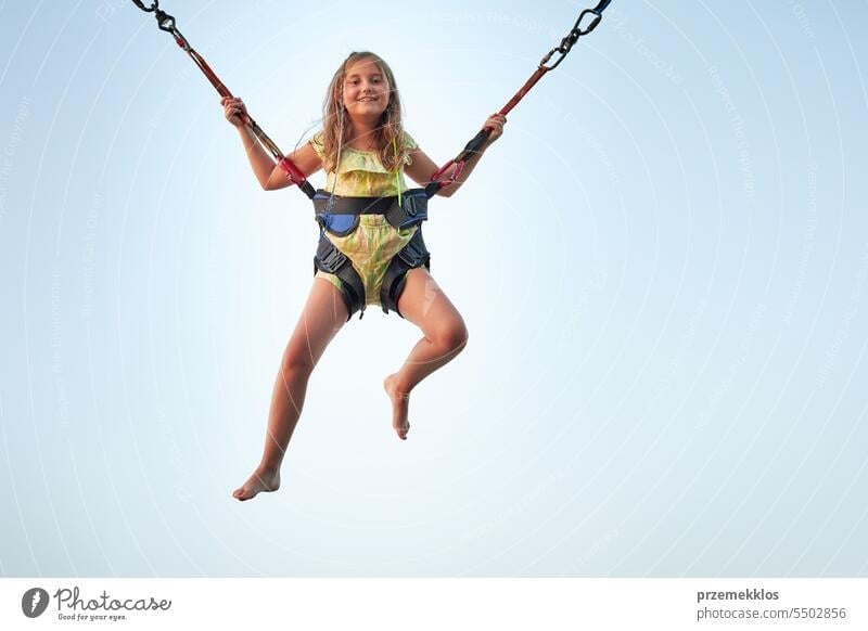 Bungee jumping at trampoline. Little girl bouncing on bungee jumping in amusement park on summer vacations playing person child fun activity sky outdoor joy