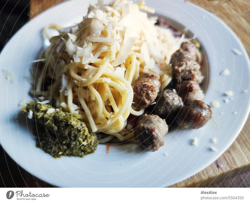 Spaghetti with sausage, parmesan flakes and green pesto on a white plate placed on a wooden cutting board pasta Noodles Dough Small sausage Fried sausages
