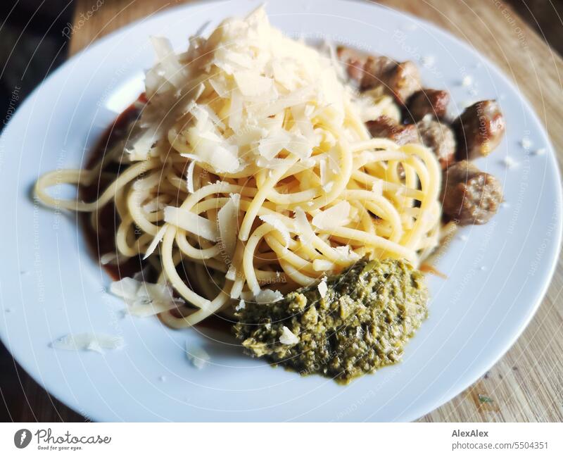 Spaghetti with sausage, parmesan flakes and green pesto on a white plate placed on a wooden cutting board pasta Noodles Dough Small sausage Fried sausages