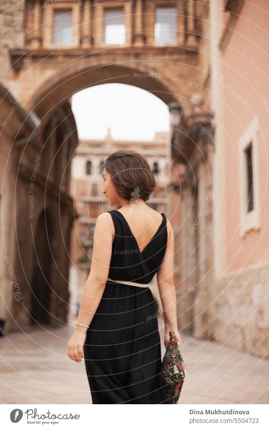 Beautiful woman from behind in little black dress at street of historic town. Gorgeous girl sightseeing in Europe. Confident woman, solo female traveler. Glamour and chic, fashion and style concept.