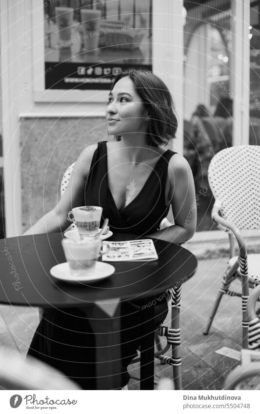beautiful woman in black dress at cafe or restaurant terrace drinking coffee. Elegant female portrait. Fashion and style concept. fashion black and white