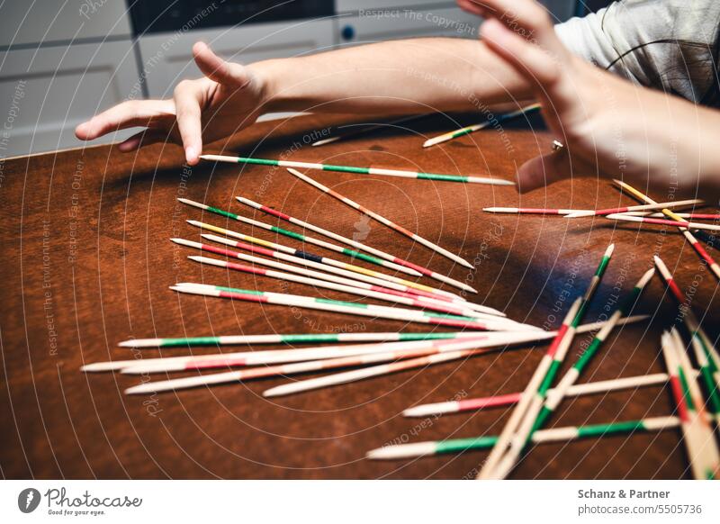 Child picks up a skewer with fingers while playing Mikado Playing wobbly cautious Family social game Infancy Fingers hands Children's game Kindergarten School