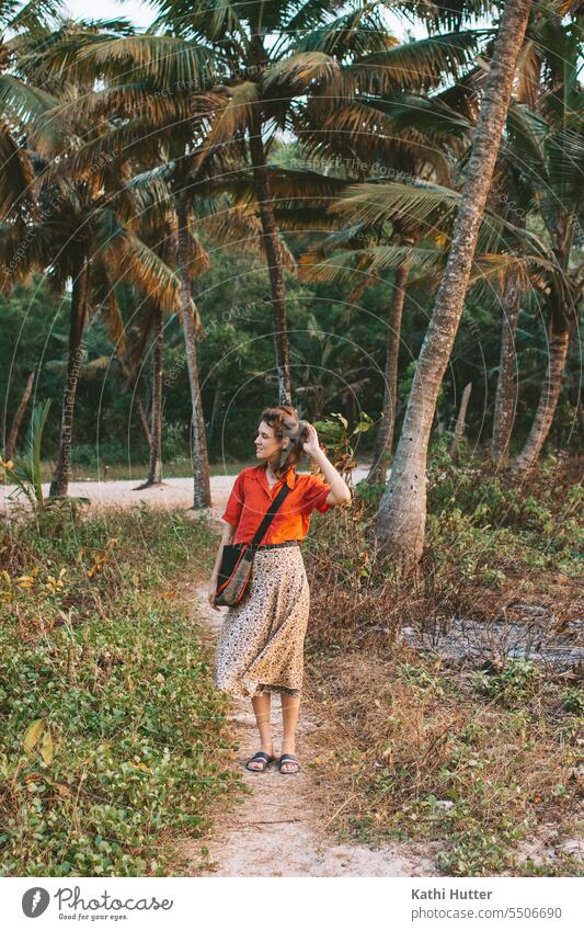 a young woman in a red blouse is standing on the beach with many palm trees in the background Woman youthful Palm tree Coconut tree Summer Tree Exotic Landscape