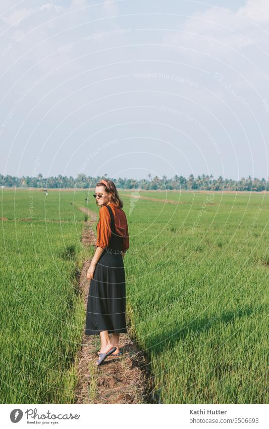 a young woman is in a rice field in Kerala, India. She is wearing a black kelid with a red blouse underneath. Woman Sunglasses Paddy field Landscape Rice Green