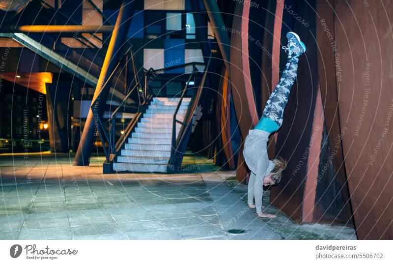 Woman doing handstand exercise against of sheet metal wall on the city at night female young woman sport posture position flexibility pilates yoga pose training