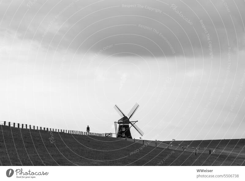 In the distance a person walks across the dike towards a windmill Minimalistic on one's own Miniature Mill Windmill traditionally Historic original Dam Dike