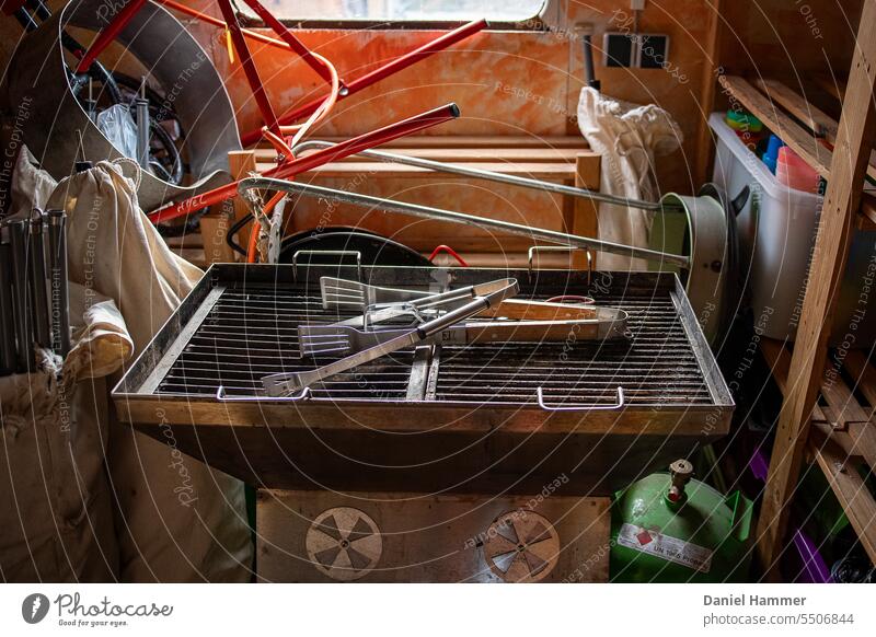 Stainless steel grill in mobile junk room with grill tongs, tents, gas bottle, garbage rack and box with drinking cups made of colorful plastic. Packed trailer for camping trip.