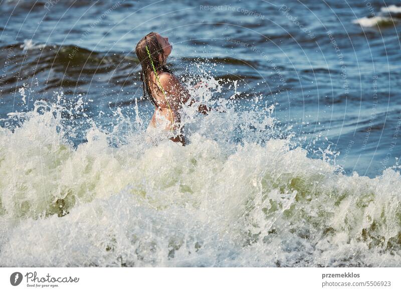 Little girl playing with waves in the sea. Kid playfully splashing with waves. Child jumping in sea waves. Summer vacation on the beach summer vacations ocean