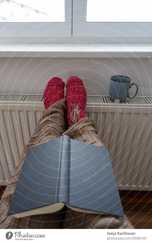 A woman with woolen socks and a woolen blanket warms herself at a radiator Woman Legs Heater Warmth Book Cozy hygge Wool socks Wool blanket Winter Cold Heating