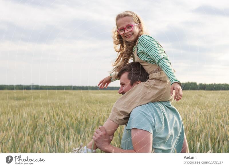 A daughter sitting on her dad's shoulders against the backdrop of a field of wheat. Happy moments in nature. Light run joy day Grow ear ears bread rye harvest