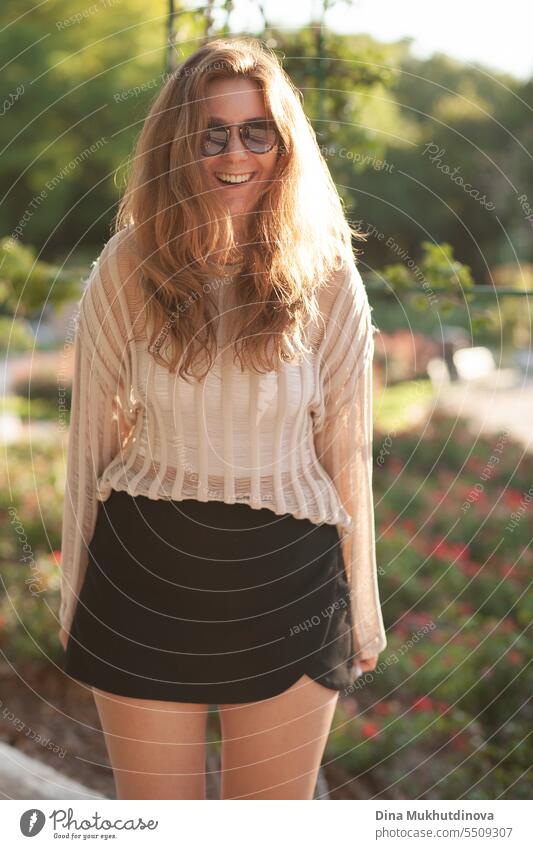 candid portrait of young beautiful woman in sunglasses laughing backlit with sunlight in summer. Pretty ginger girl with red hair. park smiling happy pretty