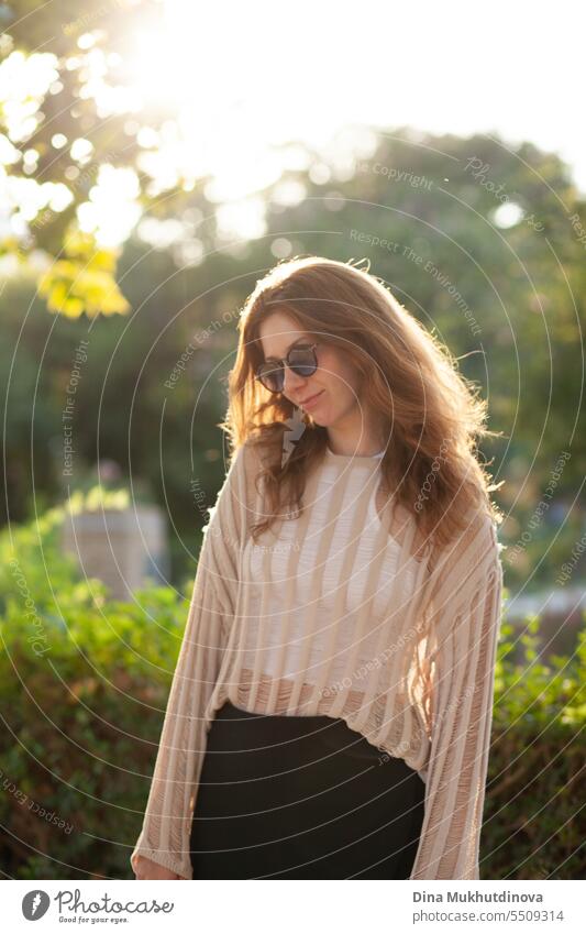 candid portrait of young beautiful woman in sunglasses backlit with sunlight in summer. Pretty ginger girl with red hair. park smiling happy pretty Smiling