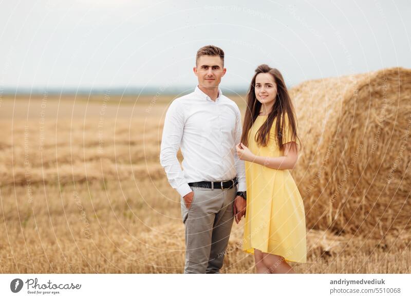 Photo of joyful couple man and woman walking through golden field with bunch of haystacks and hugging together during sunny day love young portrait countryside