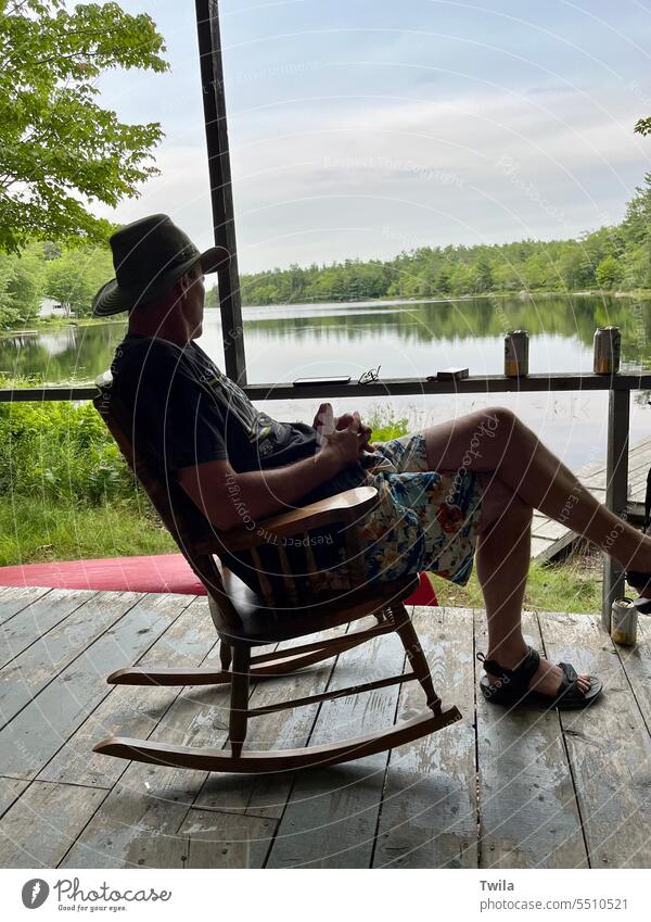 Man relaxing in rocking chair on cabin deck in front of lake Porch outdoors Rocking chair Exterior shot Lake Relaxation Summer Calm Vacation & Travel