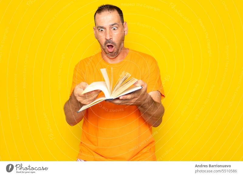 Bearded Hispanic man in his 40s turning the pages of a book visibly excited, isolated on yellow studio background. education study notebook smart surprised