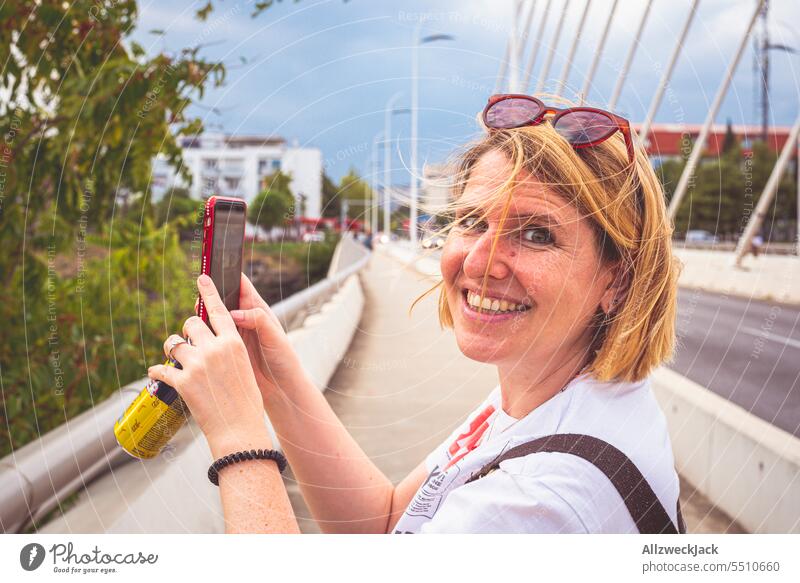 blonde middle-aged woman smiling at camera while taking photo with cell phone in Podgorica, Montenegro Middle aged woman portrait vacation Vacation photo