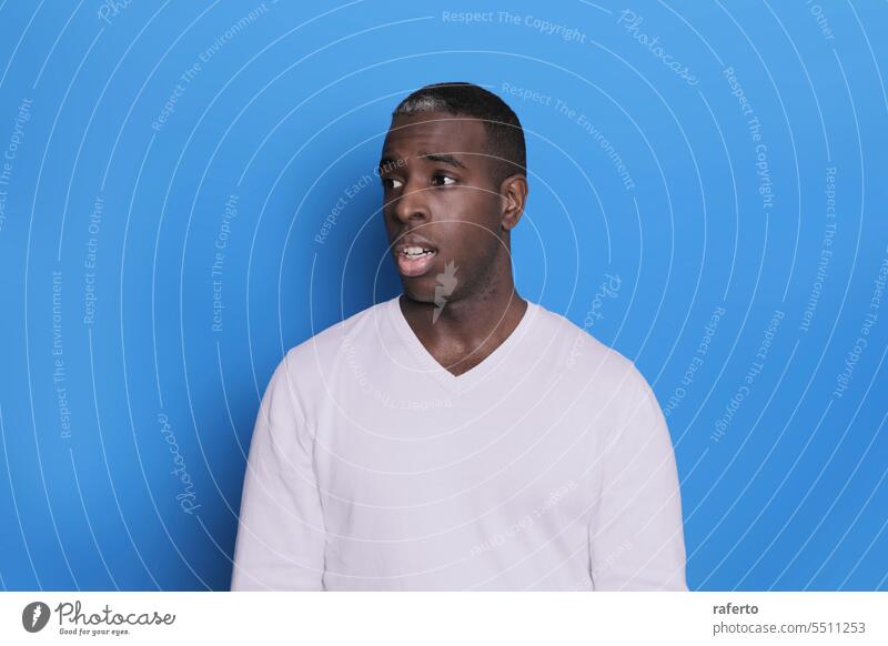 Portrait of cheerful young african-american guy wearing white casual sweater posing isolated on blue background. Carefree young millennial man aside teenage