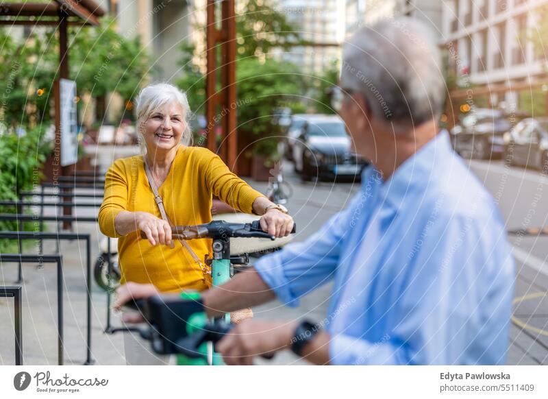 Senior couple riding electric scooters in the city people caucasian standing healthy city life gray hair enjoy street casual day portrait outside real people