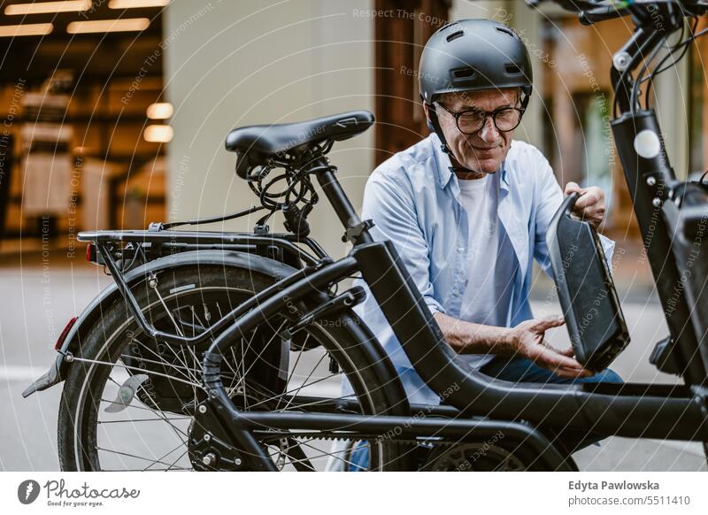 Mature man changing battery on his electric bicycle people caucasian healthy city life gray hair enjoy street casual day portrait outside real people
