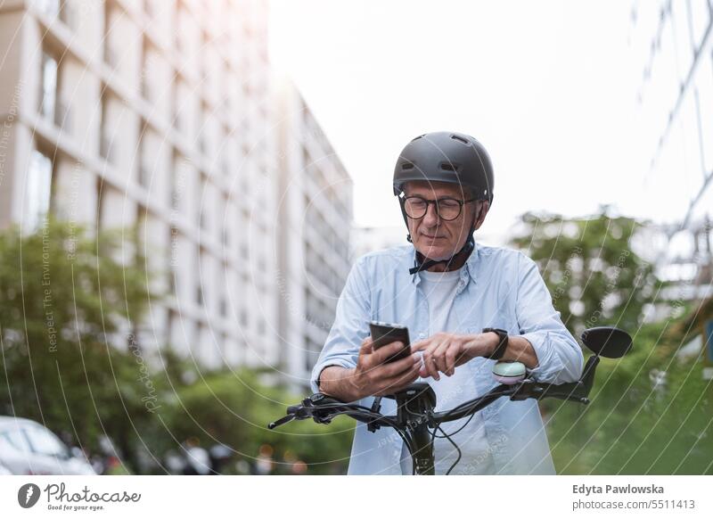 Mature man using mobile phone while riding bicycle in the city people caucasian standing healthy city life gray hair enjoy street casual day portrait outside