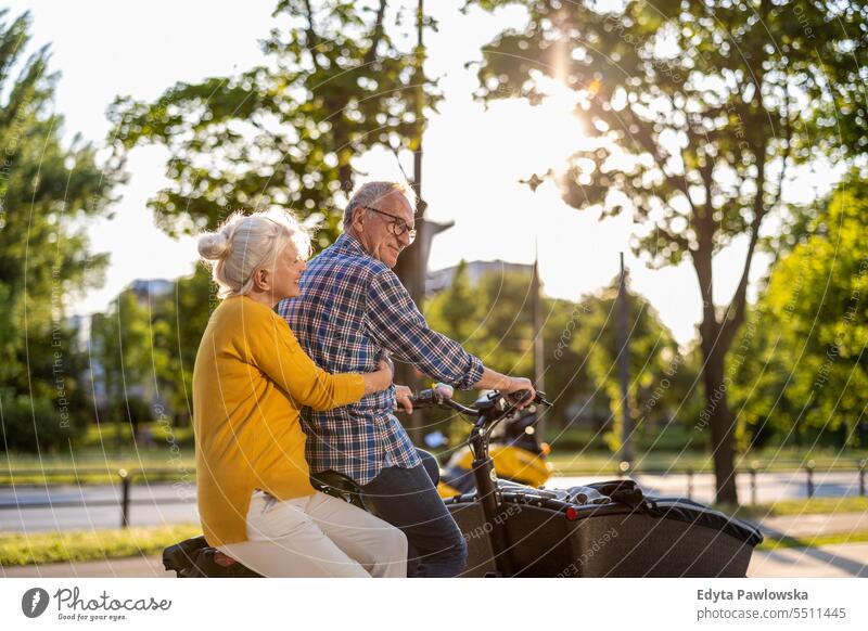 Senior couple riding cargo bike in the city people caucasian standing healthy city life gray hair enjoy street casual day portrait outside real people
