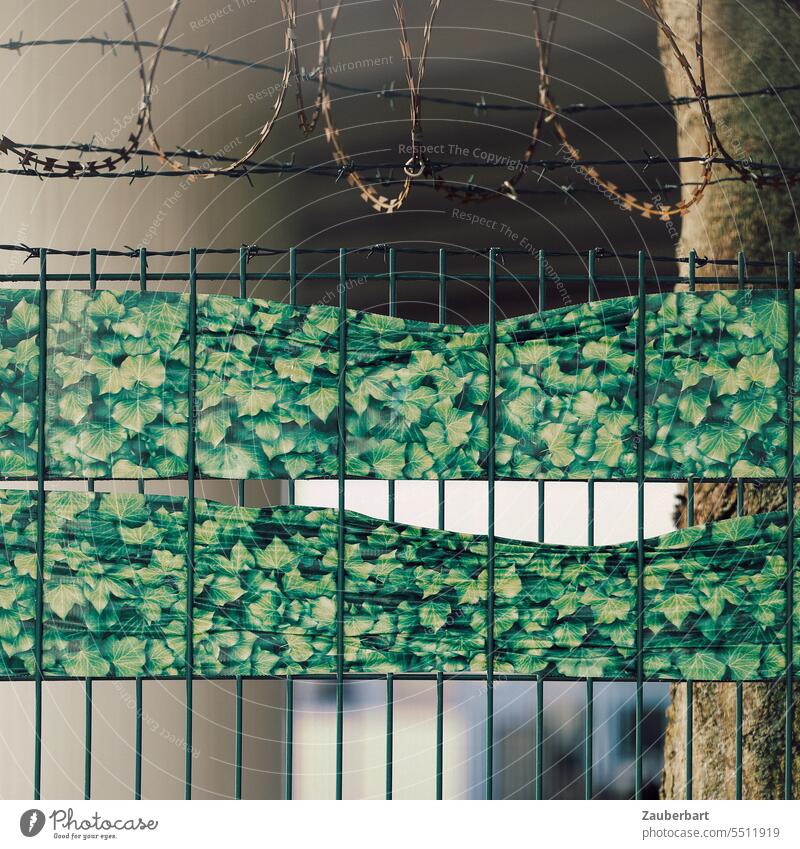 Cityscape, construction fence with barbed wire and green fake foliage, behind it concrete pillars of a bridge Town Landscape Hoarding Illusion Ki Barbed wire