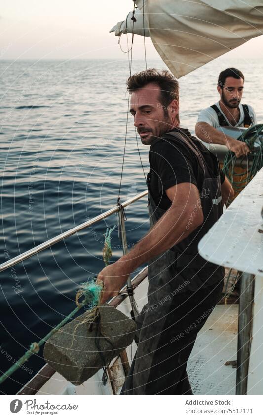 Young ethnic men standing and pulling rope of net with float on sailboat sea fishing activity seascape male young hispanic marine ocean water fisherman summer