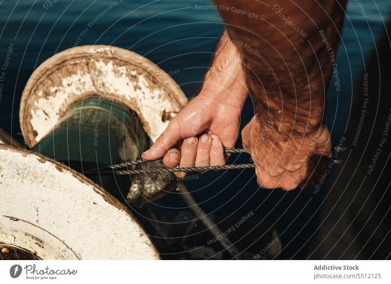 Crop man pulling fish out sea water coil rope fisher fishing marine male soller spain mallorca catch ocean equipment aqua process natural season wet hand