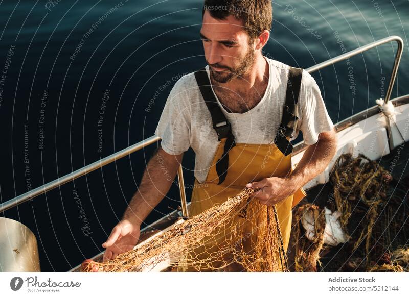 Man pulling net from sail boat in sea - a Royalty Free Stock Photo