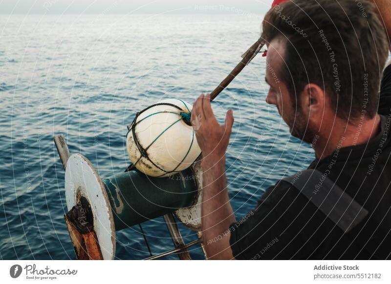 Focused ethnic man standing and releasing buoy into rippling seawater calm wheel ball equipment spiral sphere male young hispanic weather activity ocean