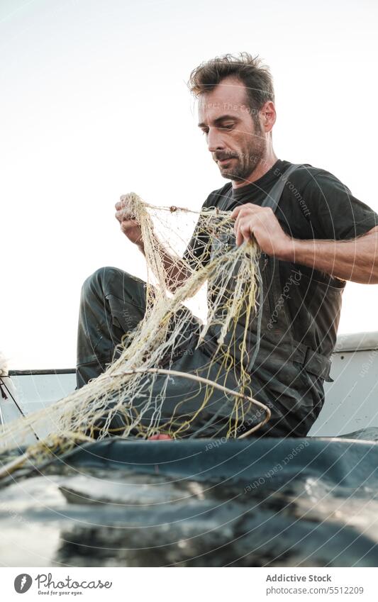 Man untangling fishing net threads to catch fish in daylight fisherman boat water deck equipment nature male transport outside wet aqua summer activity work