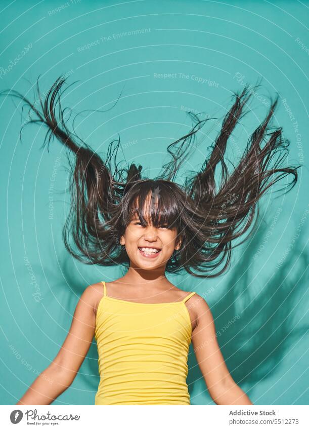 Happy ethnic girl child standing against turquoise backdrop smile kid happy cute positive joy asian childhood cheerful adorable peace glad show optimist