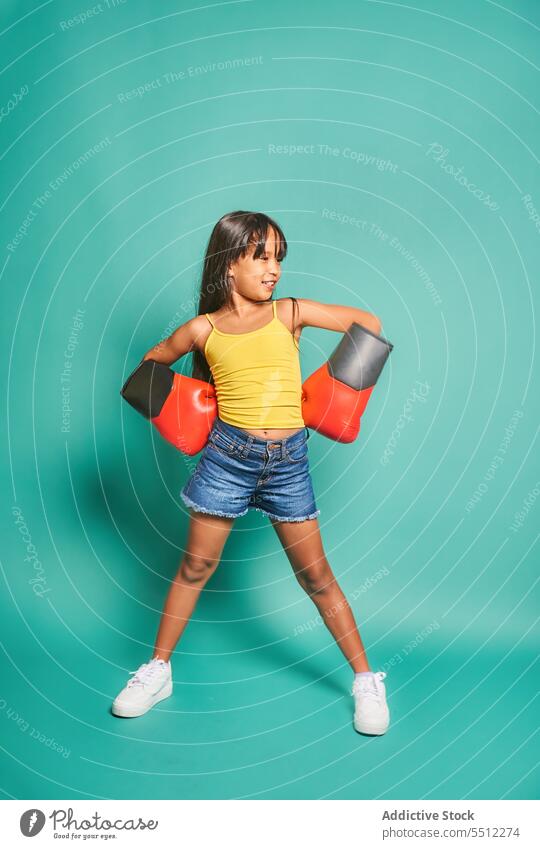 Cheerful ethnic kid girl in boxing gloves against turquoise background child smile childhood having fun happy throw playful asian sport cheerful adorable joy
