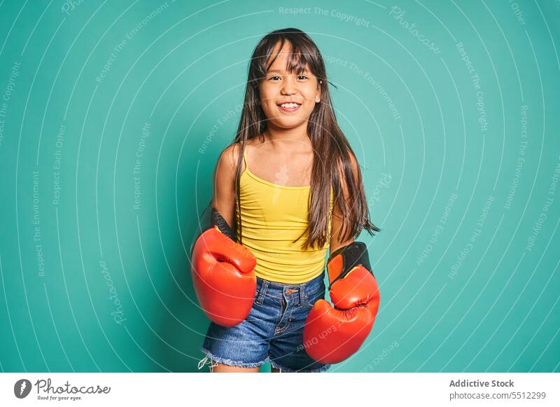 Cheerful ethnic girl child standing in boxing gloves near turquoise backdrop kid smile portrait glad positive cheerful room playful boxer appearance light
