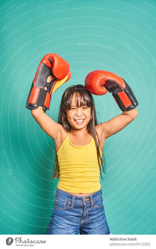 Cheerful ethnic girl child standing in boxing gloves near turquoise backdrop kid smile portrait glad positive cheerful room playful boxer appearance light