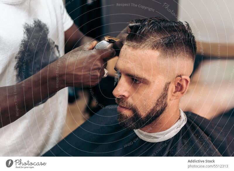 Man getting professional haircut in barbershop men client trim trimmer masculine young male multiracial african american black ethnic hairstyle cape brutal