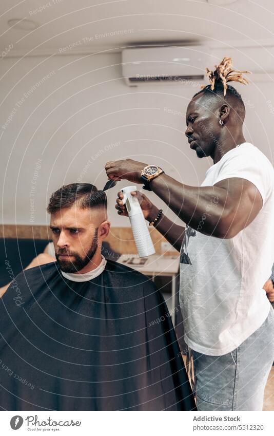 Black barber spraying water on hair of client men haircut salon barbershop sprayer masculine concentrate young male multiracial african american black wet hair