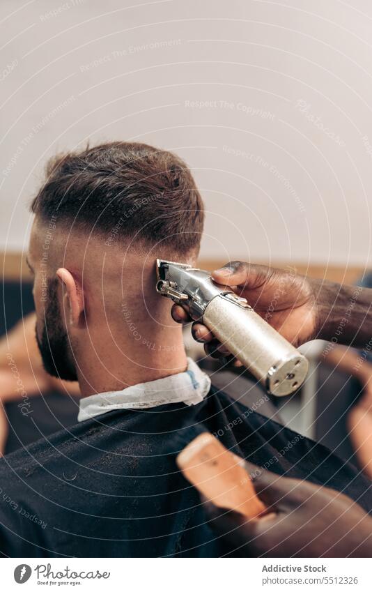 Crop barber trimming hair of male client men haircut trimmer barbershop accuracy beauty young multiracial african american black ethnic cape machine salon