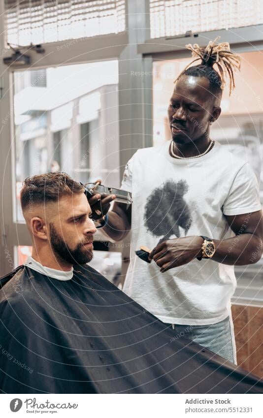 Man getting professional haircut in barbershop men client trim trimmer masculine young male multiracial african american black ethnic hairstyle cape brutal