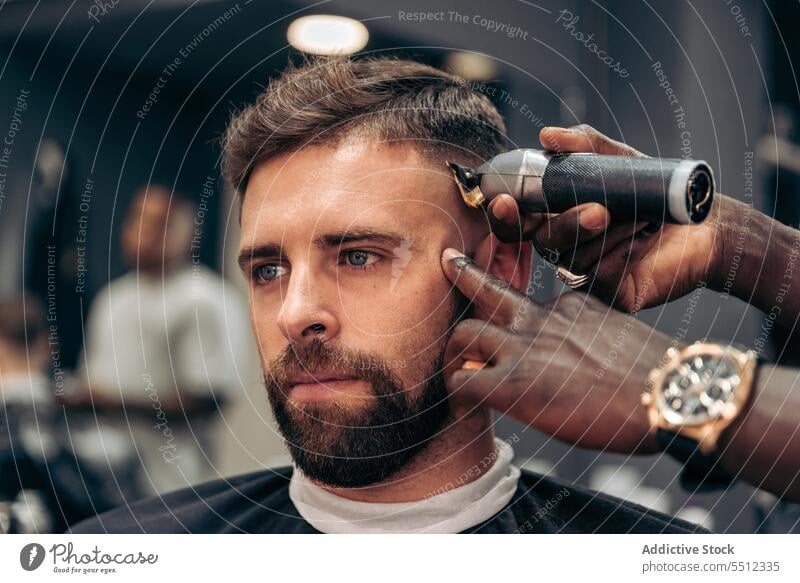 Crop barber trimming hair of male client men haircut trimmer barbershop accuracy beauty young multiracial african american black ethnic cape machine salon