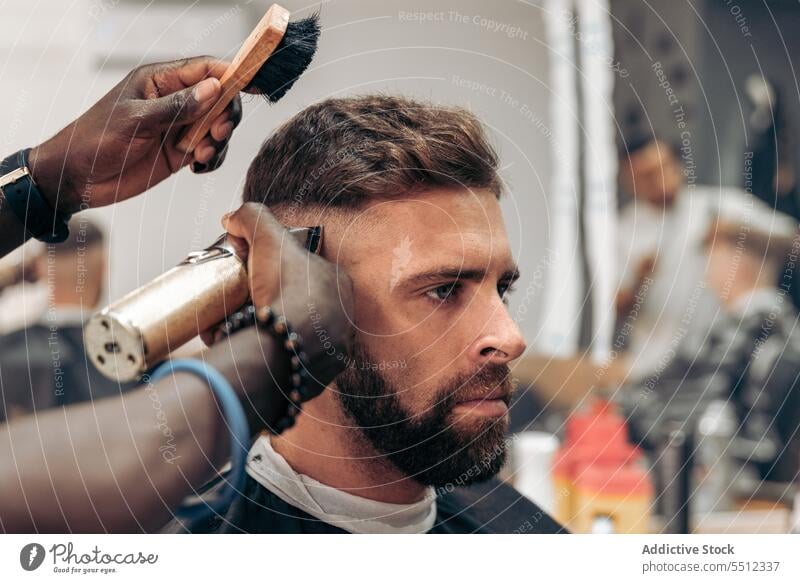 Man getting professional haircut in barbershop men client brush trim trimmer masculine young male multiracial african american black ethnic hairstyle cape
