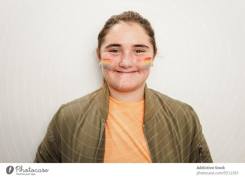 Happy young girl standing against gray wall teenage portrait paint face homosexual lgbtq smile happy glad photography colorful joy pride positive bright casual