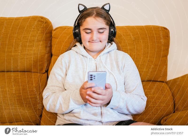 Smiling young girl with headphones and smartphone listening to music using sofa online smile happy teen teenage gadget device free time mobile living room