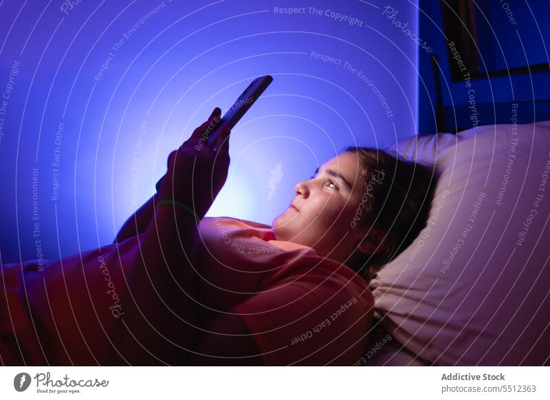 Scared young girl looking at screen lying on bed with smartphone movie scary watch teenage frighten bedroom gadget device late film video mobile entertain scare