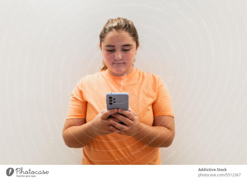 Serious young girl standing with smartphone near gray wall teenage confident using appearance serious communicate connection t shirt sleeve brown hair alone