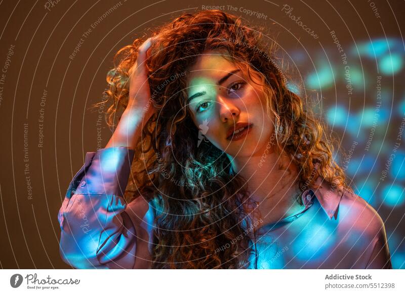 Attractive woman adjusting curly hair in room with neon lights portrait touch hair fix effect illuminate dot calm peaceful tranquil sensual young female lady
