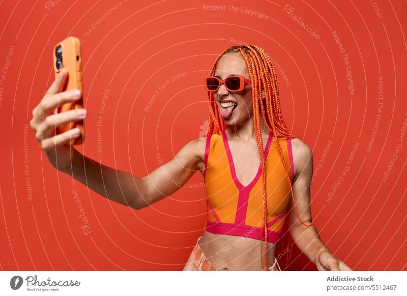 Cheerful female hipster showing tongue while taking selfie woman using smartphone show tongue take photo studio shot social media charismatic cheerful fun