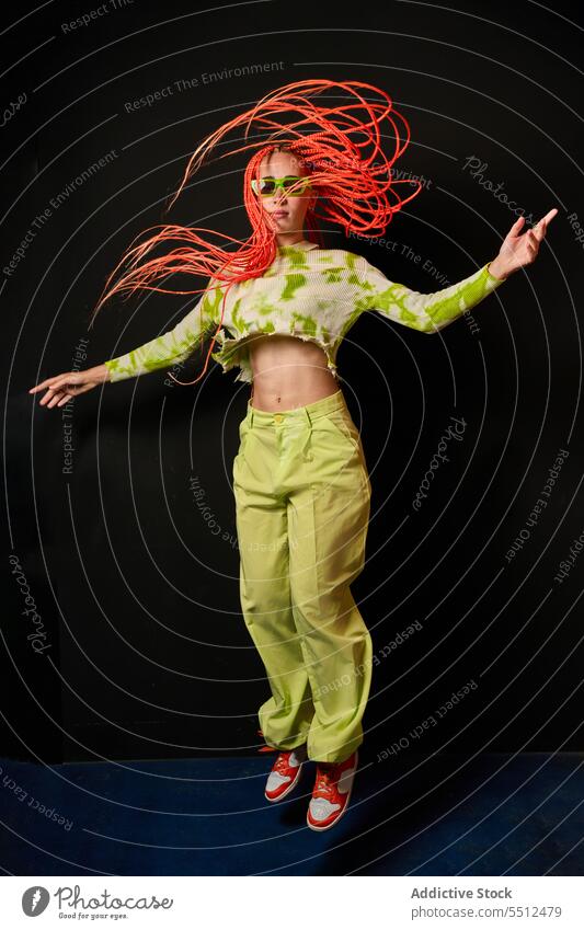 Trendy woman jumping in dark studio hipster stylish energy modern model studio shot cool flying hair young female afro braids sunglasses long sleeve top pants